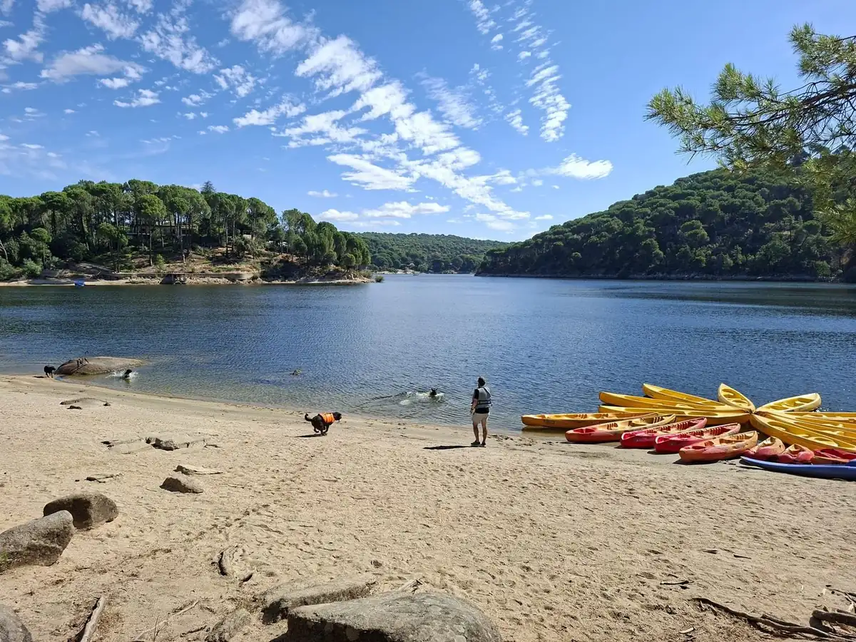 Playa de arena del Embalse de San Juan con kayaks en la orilla y un perro corriendo