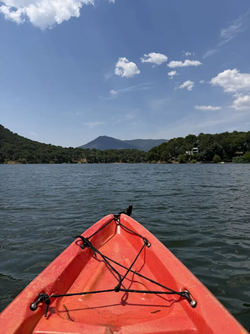 Proa de un kayak rojo apuntando al embalse con la sierra al fondo